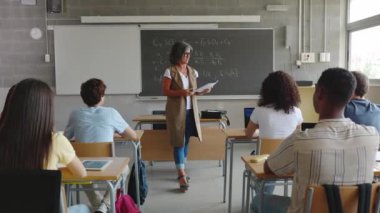 Olgun bayan öğretmen sınıfta lise öğrencilerine sınav dağıtıyor. Eğitim yaşam tarzı kavramı.