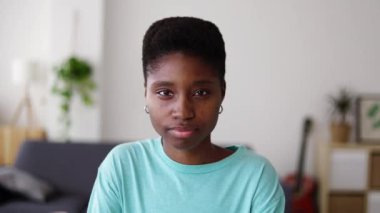 Evdeki oturma odasında kameraya bakan genç, ciddi siyahi bir kadın. Gençlik, güven ve Afrika halkı kavramı.