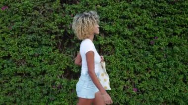 Şehir caddesinde yürüyen çok kültürlü genç bir kadının yan görüntüsü. Neşeli milenyum dişisi yazın açık havada yürüyüş yapıyor. İnsanlar ve mutluluk kavramı.