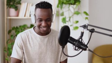 Mutlu genç Afrikalı adam evden canlı yayın yapıyor. Küçük yayın stüdyosundaki profesyonel mikrofonu kullanarak içerik yaratıcısı radyo programını kaydediyor.