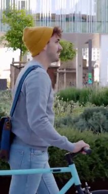 Bisikletle kampüsten ayrılan mutlu genç bir öğrencinin dikey HD videosu. Eğitim, insanlar ve çevre dostu ulaşım kavramı. Yan görünüm.