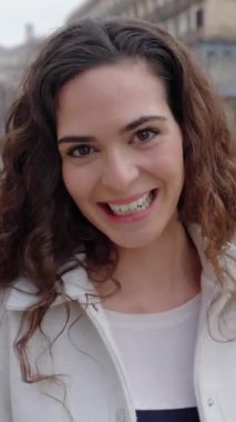 Dikey HD video görüntülerinde gülümseyen yetişkin bir kadın kameraya bakıyor. Şehir caddesinde kendini pozitif hissediyordu.