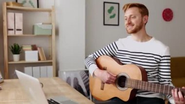 Evden uzakta bilgisayar öğretmeniyle çevrimiçi müzik sınıfında gitar öğrenen bir adam - Genç yetişkin dizüstü bilgisayarla müzik öğretiyor - Uzaktan eğitim kavramı