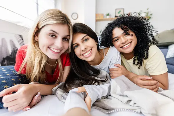 Pijamalı üç mutlu genç kız evde pijama partisi sonrası şiltede uzanmış selfie çekiyorlar.