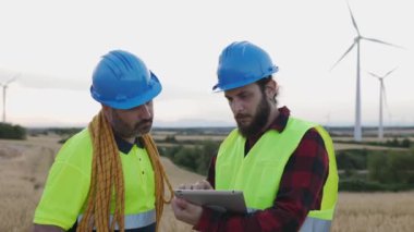 Teknisyenler rüzgâr tarlasında dijital tablet kullanıyorlar. Yenilenebilir ve alternatif enerji kavramı