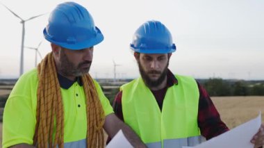 Rüzgar türbini çiftliğinde çalışan iki genç bakım mühendisi. Profesyonel teknisyen erkekler elektrik santrali inşaatı hakkında tartışıyorlar.