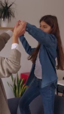 Genç Latin annenin evdeki kanepede kızıyla dans edişinin dikey videosu. Çok ırklı aile haftasonu oturma odasında eğleniyor.. 