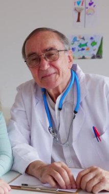 Tıbbi konsültasyon sırasında kameraya gülümseyen kıdemli doktor erkek portresi. Hastanedeki hastanın yanında duran mutlu çocuk doktoru. Sağlık ve insan hakları kavramı.