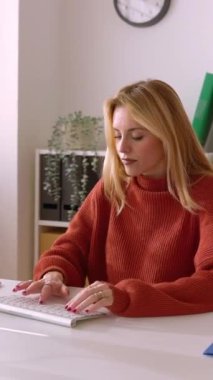 Ofiste oturan çekici genç iş kadınının dikey HD videosu. Milenyum girişimcisi kadın modern işyerinde online olarak çalışmaya ara veriyor..