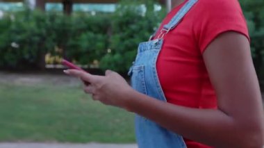 Şehir caddesinde cep telefonu kullanan genç kadın elleri yakından görülüyor. Z Gen kızı yazın dışarıda akıllı telefon uygulamasından mesaj yolluyor. Teknoloji yaşam tarzı ve sosyal medya kavramı.