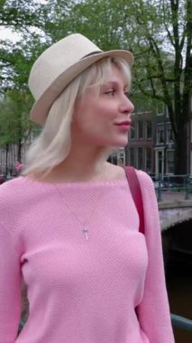 Amsterdam 'da yürüyen mutlu genç bayan turistin yavaş çekim dikey HD videosu. Güzel bir milenyum kadını yaz tatilinde Hollanda 'yı geziyor. Seyahat yaşam tarzı konsepti.