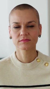 Laptop 'taki iş arkadaşını dinleyen yetişkin bir kadının ev ofisinden çekilmiş dikey HD videosu. Tıraşlı saçlı bir iş kadını iş arkadaşlarıyla internette konuşuyor..