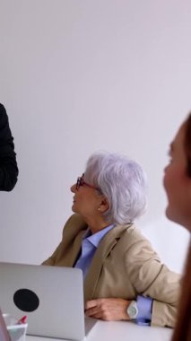 Genç işadamının ofis işyerindeki toplantı odasında şirket çalışanlarına sunum yaptığı dikey HD videosu. Takım çalışması, işbirliği ve ortaklık kavramı.