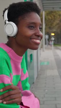 Şehirdeki tramvayda bekleyen kulaklıklı genç Afrikalı kadının dikey HD videosu.. 