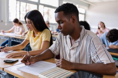 Lise öğrencileri sınıfta deftere yazı yazıyorlar. Genz sınıf arkadaşları sınıfta masa başında egzersiz yapıyorlar. Eğitim yaşam tarzı kavramı.