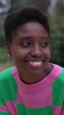 Gülümseyen Afrikalı genç bir kadının şehir merkezinde otururken çekilmiş dikey HD videosu. Mutlu insanlar konsepti.