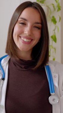 Masada oturan genç bayan doktorun gülümseyen portresi. Hasta bakış açısına göre doktor çevrimiçi danışma. Dikey HD video veya telefon ekranı görüntüsü