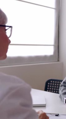 Tıp merkezindeki danışmanlık sırasında genç hastaları dinleyen yaşlı kadın doktorların dikey HD videosu. Sağlık hizmeti yaşam tarzı konsepti. Arka görünüm.