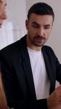 Ofiste dizüstü bilgisayarla çalışırken tartışan iki genç iş arkadaşının dikey HD videosu. Takım çalışması ve işbirliği kavramı.