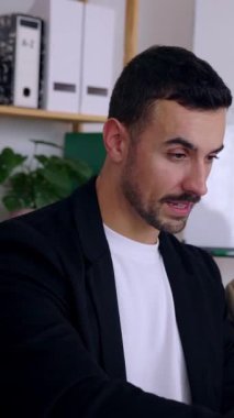 Genç iş adamının ofiste iş stratejisi ya da kadın iş arkadaşlarıyla plan tartışırken dizüstü bilgisayarda çalıştığı dikey HD videosu. Takım çalışması ve profesyonel iş adamları kavramı.