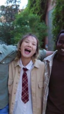 Dışarıda kameraya doğru yürürken birbirine sarılan mutlu çok ırklı grubun dikey HD videosu. Birleşmiş Milenyum öğrenci çeşitliliği şehir sokaklarında eğlenirken birlik gösteriyor. 