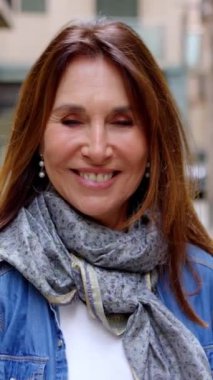 Şehir caddesinde kameraya bakan orta yaşlı güzel bir kadının dikey HD video portresi..