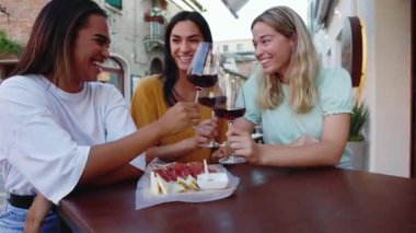 Üç tane çok ırklı genç kadın yaz tatilinde restoranın masasında oturmuş kırmızı şarap içiyorlar. Kadın arkadaşlığı ve tatil yaşam tarzı konsepti.