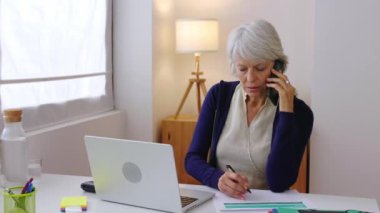 Başarılı bir orta yaşlı iş kadını. Ev telefonuyla konuşurken dizüstü bilgisayar kullanıyor. İş ve güçlendirme konsepti. Yüksek kalite 4k görüntü. 