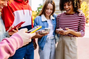 Açık havada cep telefonu kullanan bir grup mutlu genç arkadaş. Erkek ellerine akıllı telefon cihazına odaklan.