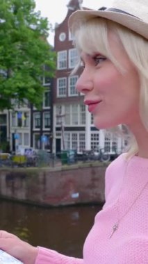 Amsterdam 'ı gezen çekici genç bir bayan turist. Hollanda 'da tatilin tadını çıkaran yaz şapkalı genç bir kadın. Seyahat ve tatil yaşam tarzı kavramı. VERTICAL HD VIDEO.