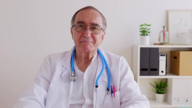 Tıbbi konsültasyonda masada kameraya gülümseyen mutlu erkek doktorun portresi.