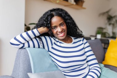 Evdeki kanepede dinlenen güzel siyah bir kadının portresi. Bin yıllık siyah Latin Amerikalı kızın kameraya gülümseyişinin iç yüzü..