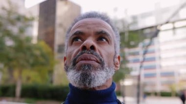 Şehir caddesinde dikilen yaşlı Latin Amerikalı adamın portresi. Olgun bir erkeğin finans bölgesinde açık havada düşüncelere daldığı bir fotoğraf. İş insanları kavramı.