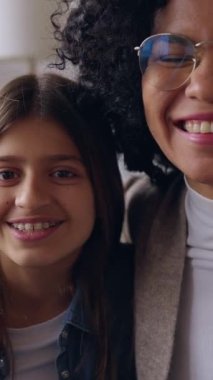 Neşeli Latin kadının evdeki kanepede oturan kızıyla telefonda görüntülü konuşma yaptığı dikey HD video. Anne ve çocuk birlikte eğleniyorlar. Tek ebeveynli aile kavramı. Bakış açısı.