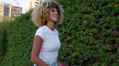 Heyecanlı, Afro-Amerikan bir kadının şehir caddesinde dans ederken telefonla müzik dinlemesinin yan görüntüsü. Tasasız, kutlama ve mutluluk konsepti