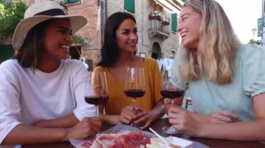 İtalya 'da yaz tatili boyunca restoranda kırmızı şarap içip eğlenen üç farklı kadın. Arkadaşlık, rahatlık ve seyahat konsepti.
