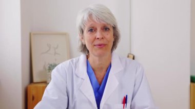 Olgun sağlık çalışanlarının POV 'u tıbbi odadan video görüşmesi yapıyor. Mavi önlüklü ve ceketli orta yaşlı kadın hemşire hastayla sanal konferans aracılığıyla konuşuyor. Teletıp kavramı.