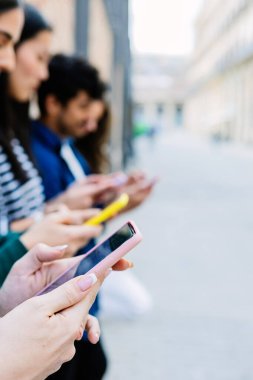 Şehir caddesinde cep telefonu kullanan genç insanların dikey görüntüsü. Sosyal medya ve teknoloji yaşam tarzı kavramı. Ellere odaklan. Metin için alanı kopyala