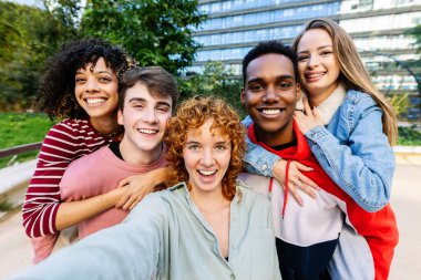 Genç ve mutlu bir grup öğrenci kampüsün önünde selfie çekerken eğleniyor. Arkadaşlık ve gençlik kavramı