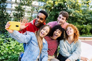 Bir grup genç, kenar mahallede boş vakit geçirirken birlikte oturup selfie çektirirken eğleniyor. Gen Z öğrencileri kampüs üniversitesinde poz veriyor..