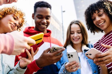 Dışarıda duran cep telefonu cihazını kullanan bir grup genç arkadaş. Z jenerasyonu kızları ve erkekleri akıllı telefon uygulamasında sosyal medya içeriğini izlerken eğleniyorlar. Teknoloji konsepti. Telefonlara odaklan.