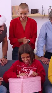 Heyecanlı genç kızın ailesiyle birlikte Noel hediyesini açtığı dikey HD video. Çok nesilli aile Noel 'i kutluyor. Oturma odasındaki kanepede oturuyorlar..