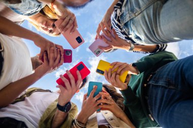 Genç arkadaşların akıllı telefonları tutup cep telefonu cihazlarında içeriklerini gösterdikleri düşük açılı bir bakış açısı. Gençlik ve teknoloji yaşam tarzı konsepti