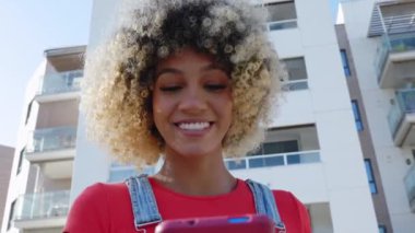 Genç Latin Amerikalı kadın şehir binaları üzerinde cep telefonu kullanıyor. Milenyum kızı dışarıda cep telefonu uygulamasından sosyal medya içeriğini izliyor. Teknoloji yaşam tarzı ve sosyal medya kavramı.