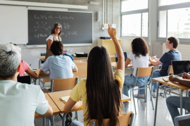 Genç nesil z öğrencileri lisede derse katılıyor. Bayan öğrencinin ders sırasında kıdemli bayan öğretmene soru sorması. Eğitim konsepti. Kaldırılmış ele odaklan.