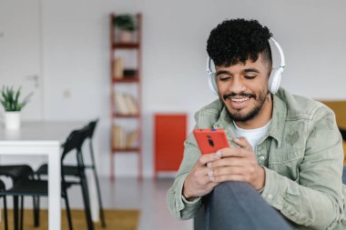 Mutlu genç adam evdeki kanepede dinlenirken cep telefonu kullanıyor. Teknoloji konsepti.