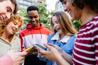 Cep telefonu uygulamasından komik içerikler izleyen çok ırklı gençler. Milenyum çeşitliliği olan arkadaşlar dışarıda akıllı cep telefonu cihazları kullanarak eğleniyorlar. Gençlik ve teknoloji kavramı