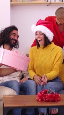 Mutlu aile Noel 'i birlikte kutlarken çekilmiş dikey HD videosu. Noel Baba şapkalı güzel bir kadın Noel arifesinde evde açılış hediyesi veriyor..