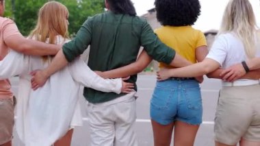 Farklı insanların birbirine sarıldığı arka plan görüntüsü. Birleşmiş Milenyum dostları birlikte yürüyorlar. Şehir sokağındaki kameradan uzaklaşıyorlar. Çeşitlilik, toplum ve arkadaşlık kavramı.