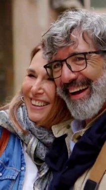 Dikey HD video: Şehir caddesinde birlikte gülen yaşlı ve çekici bir çiftin portresi. Emekli insanlar dışarıda kaynaşıyor..